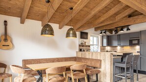 Une cuisine moderne avec des poutres en bois, un coin repas avec une table et des chaises en bois, et une guitare accrochée au mur.