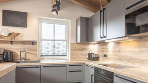 Une cuisine moderne avec des meubles gris, un plan de travail en bois, une fenêtre et des appareils électroménagers intégrés.