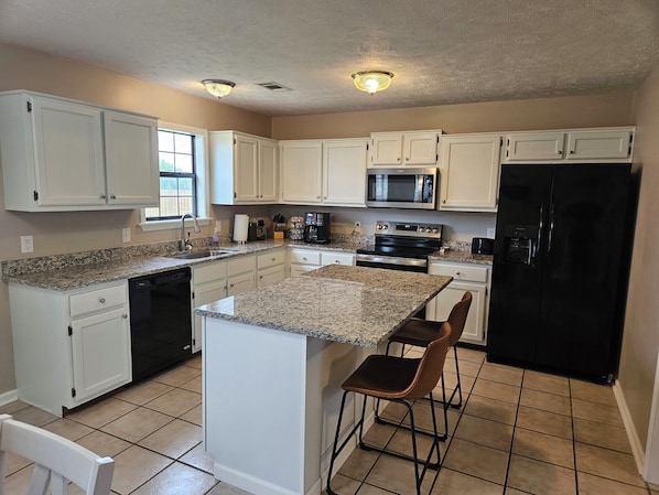 A kitchen with white cabinets, a granite countertop, a black refrigerator, and a stainless steel stove.