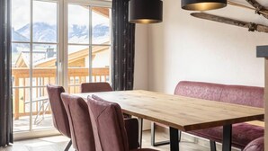 Een eetgedeelte met een houten tafel, stoelen met kussens en een bankje. Twee hanglampen hangen aan het plafond.