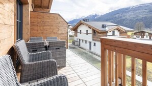Een houten balkon met rieten meubilair, met uitzicht op een bergachtig landschap.