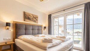 Een hotelkamer met een groot bed, een nachtkastje, een wandlamp en een raam met uitzicht op bergen.