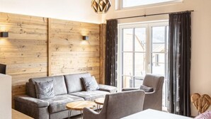 Een moderne woonkamer met een grijze bank, een houten accentmuur en een groot raam met gordijnen.