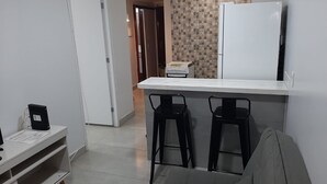 A compact kitchen with a white countertop, two black bar stools, and a refrigerator. - Apartamento 2010 (Setor Central Goiânia)