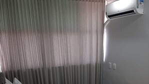 A hotel room with a bed, a window with curtains, an air conditioning unit, and a towel on the bed. - Apartamento 2010 (Setor Central Goiânia)