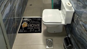 Un baño con paredes de mármol, inodoro, ducha y un estante pequeño.