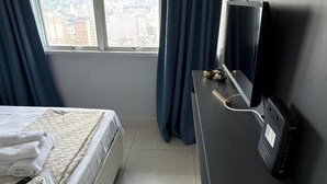 Una habitación de hotel moderna con cama, escritorio con computadora, televisión y un gran ventanal con cortinas.