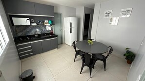 Una cocina moderna con armarios grises, encimera negra y refrigerador blanco. Hay una mesa de comedor con sillas y una pequeña planta en maceta.
