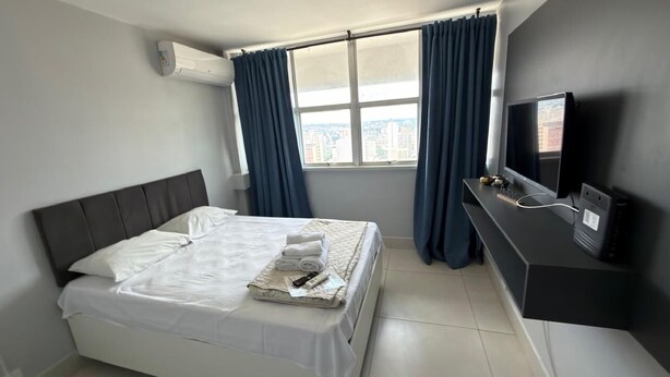 Una habitación de hotel con cama, televisión y ventana con cortinas.