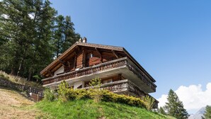 Un chalet de madera tradicional con balcón, situado en una ladera con cielo despejado.