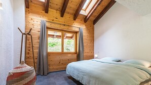 Un dormitorio con techo de madera, un ventanal grande, una cama y una lámpara colgante.