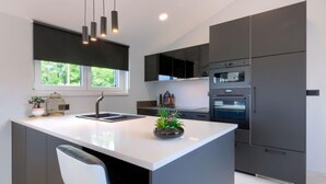 Une cuisine moderne dotée d’un îlot central, de meubles de rangement aux couleurs sombres et d’une grande fenêtre.
