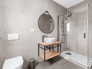 Un baño moderno con inodoro, lavabo, espejo y cabina de ducha de vidrio.