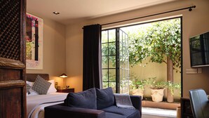 Een slaapkamer met een bed, een donkere bank, een televisie en een groot raam met uitzicht op groen.