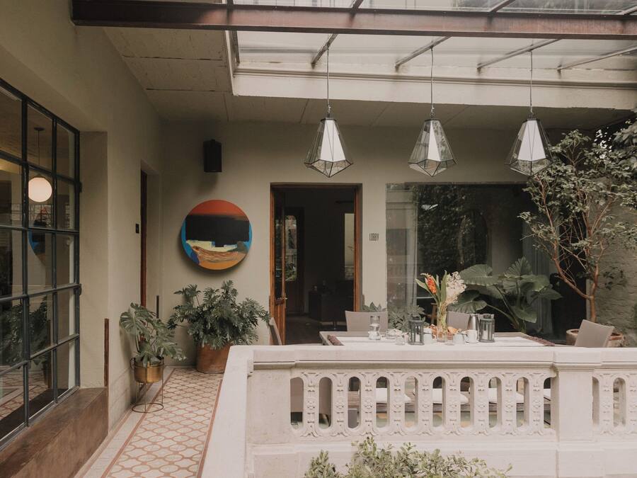 Un área de estar moderna al aire libre con barandilla de vidrio, plantas en macetas y vistas del interior.