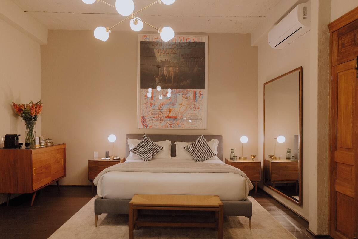 A bedroom with a bed, bedside tables, a mirror, and a wall-mounted poster.