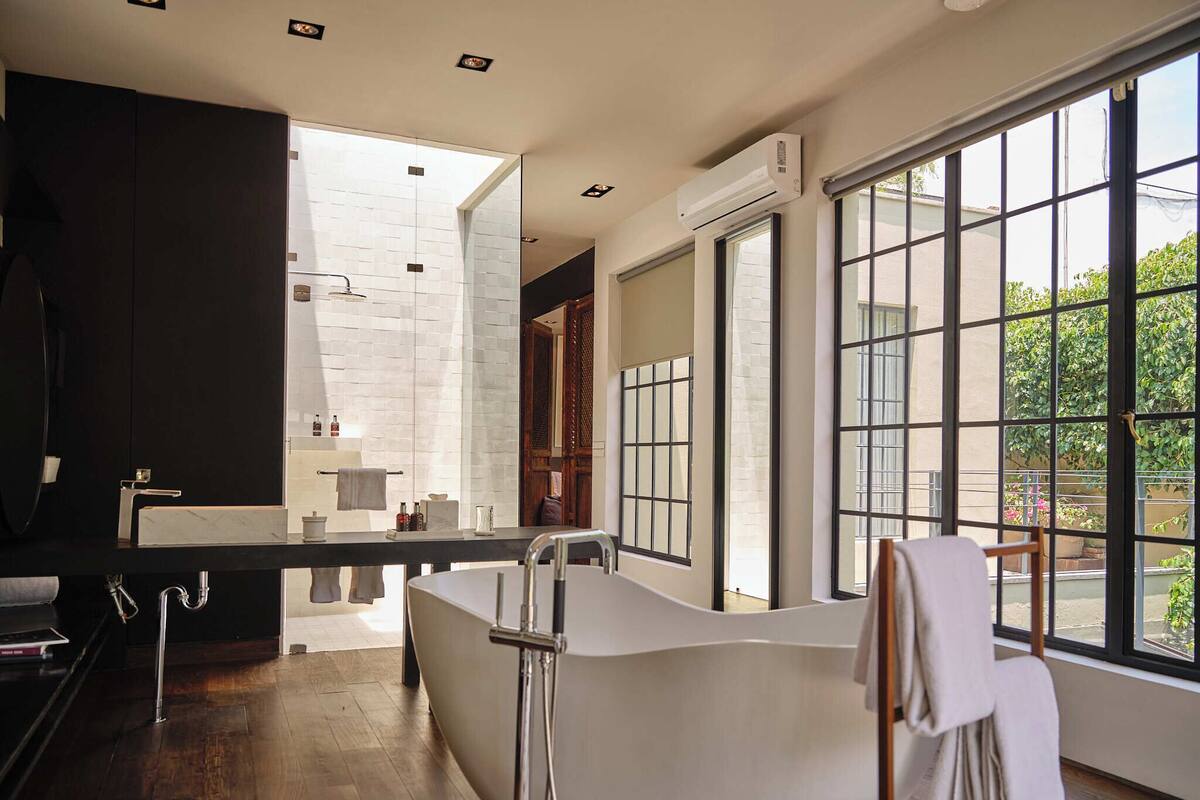 A modern bathroom with a large bathtub, a vanity with a mirror, and a window providing a view of greenery outside.