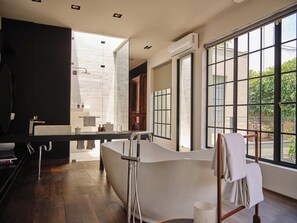 A modern bathroom with a large bathtub, a vanity with a mirror, and a window providing a view of greenery outside. - Casa Seis Siete (Mexico City)