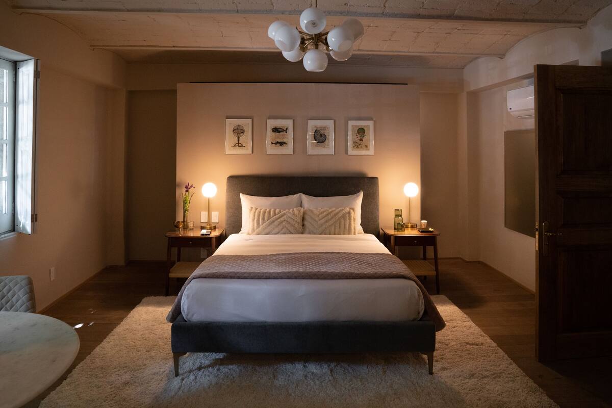 A bedroom with a large bed, bedside tables, a chandelier, and artwork on the wall.