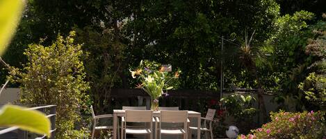 An outdoor seating area with a table and chairs, surrounded by potted plants and trees.