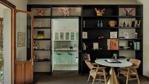 Een modern interieur met een eethoek, open wandplanken met decoratieve objecten, en uitzicht op een keuken.