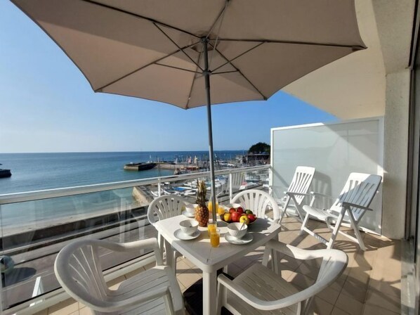 A balcony with a table set for breakfast, white chairs, and a large umbrella.