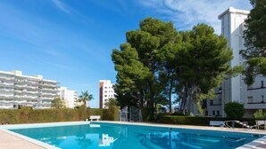Una piscina rectangular con plataforma de baldosas, rodeada de árboles y edificios modernos.