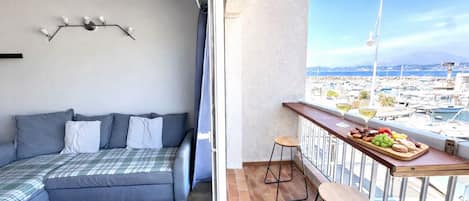 A balcony with a view of a marina, a sofa with pillows, and a table with food and drinks.