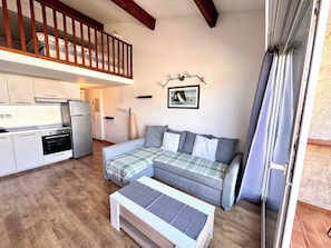 A compact living space with a kitchenette, a sofa, a coffee table, and a balcony with a sliding door.