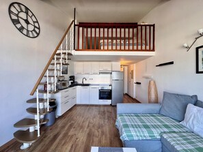 A compact living space with a loft bedroom, kitchenette, and a staircase.