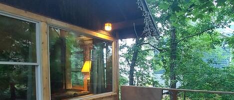 Eine Holzterrasse mit einer Bank, einem Fenster mit Lampe und Blick auf Bäume.