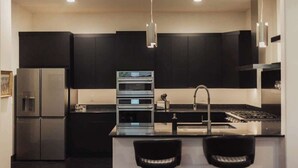 A modern kitchen with a central island, stainless steel appliances, and black cabinetry. - Renovated & Modern 8 Guest Stay - Midtown Billings (Billings)