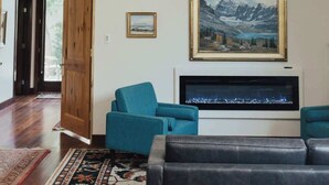 A living room with a ceiling fan, a fireplace, a large framed painting, and a television. - Renovated & Modern 8 Guest Stay - Midtown Billings (Billings)