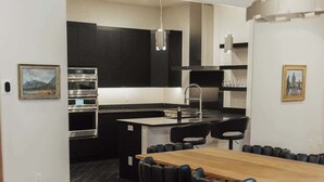 A modern kitchen with built-in appliances, a dining area with a wooden table and black chairs, and a patterned rug. - Renovated & Modern 8 Guest Stay - Midtown Billings (Billings)