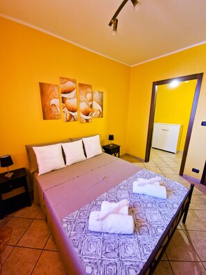 Camera d'albergo con un letto grande, un comodino, una lampada a parete e una porta che dà su un bagno.