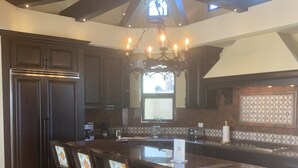 A kitchen with dark wooden cabinets, a central island with bar stools, a chandelier, and a large window. - Vacations smutny 
 (Cabo San Lucas)