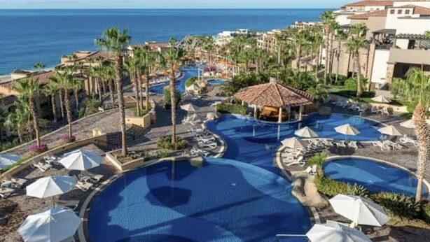 A resort with multiple swimming pools, palm trees, and a view of the ocean. - Vacations smutny 
 (Cabo San Lucas)