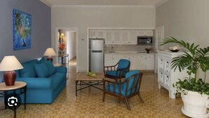 A living room with a blue sofa, a coffee table, and a dining area with two blue chairs. A kitchen with white cabinets and appliances is visible in the background. - Vacations smutny 
 (Cabo San Lucas)