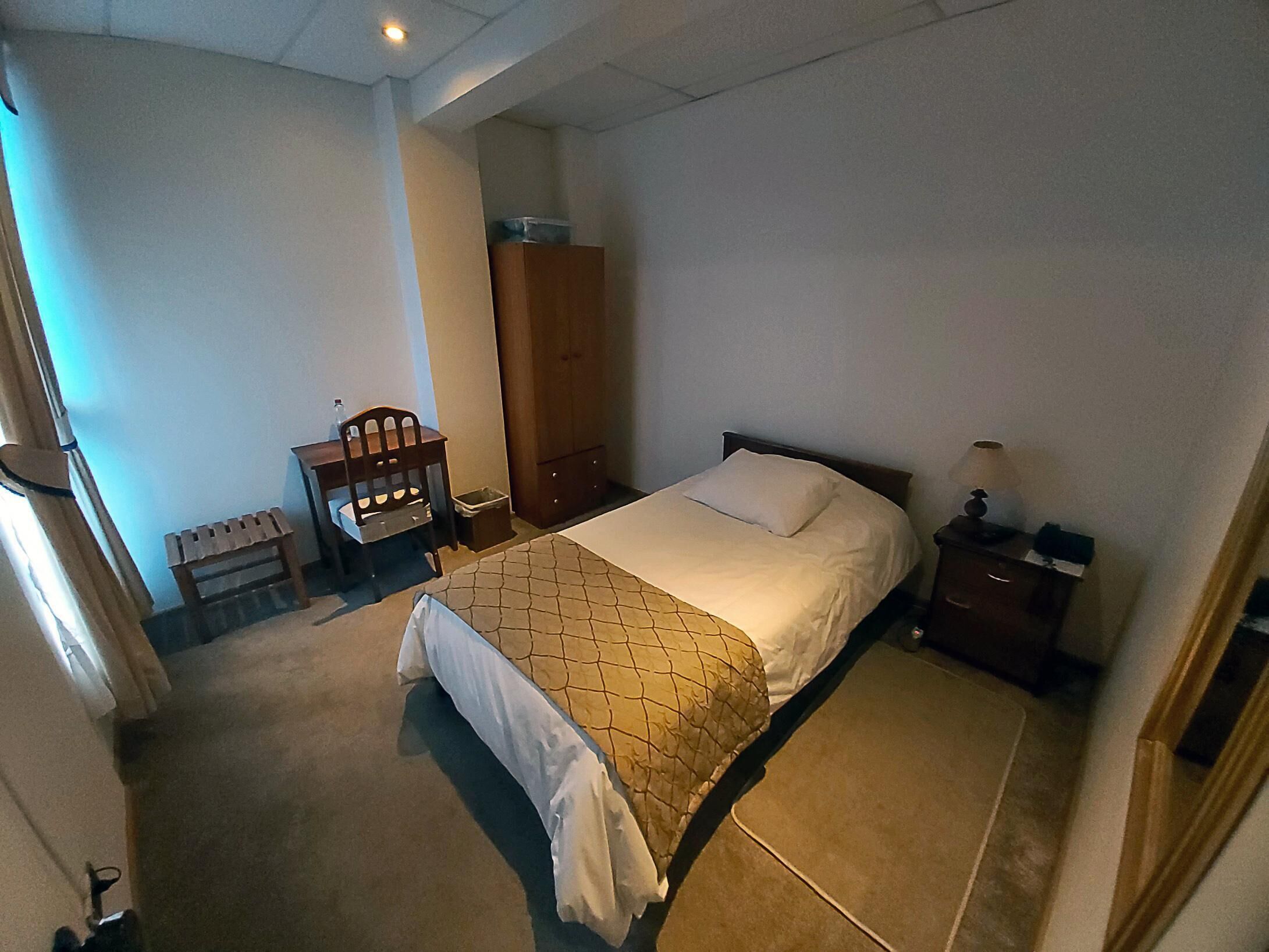 A bedroom with a bed, a wooden chair, a nightstand, and a wardrobe.