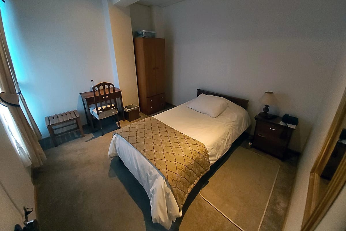 Un dormitorio con una cama, una silla de madera, una mesita de noche y un armario.