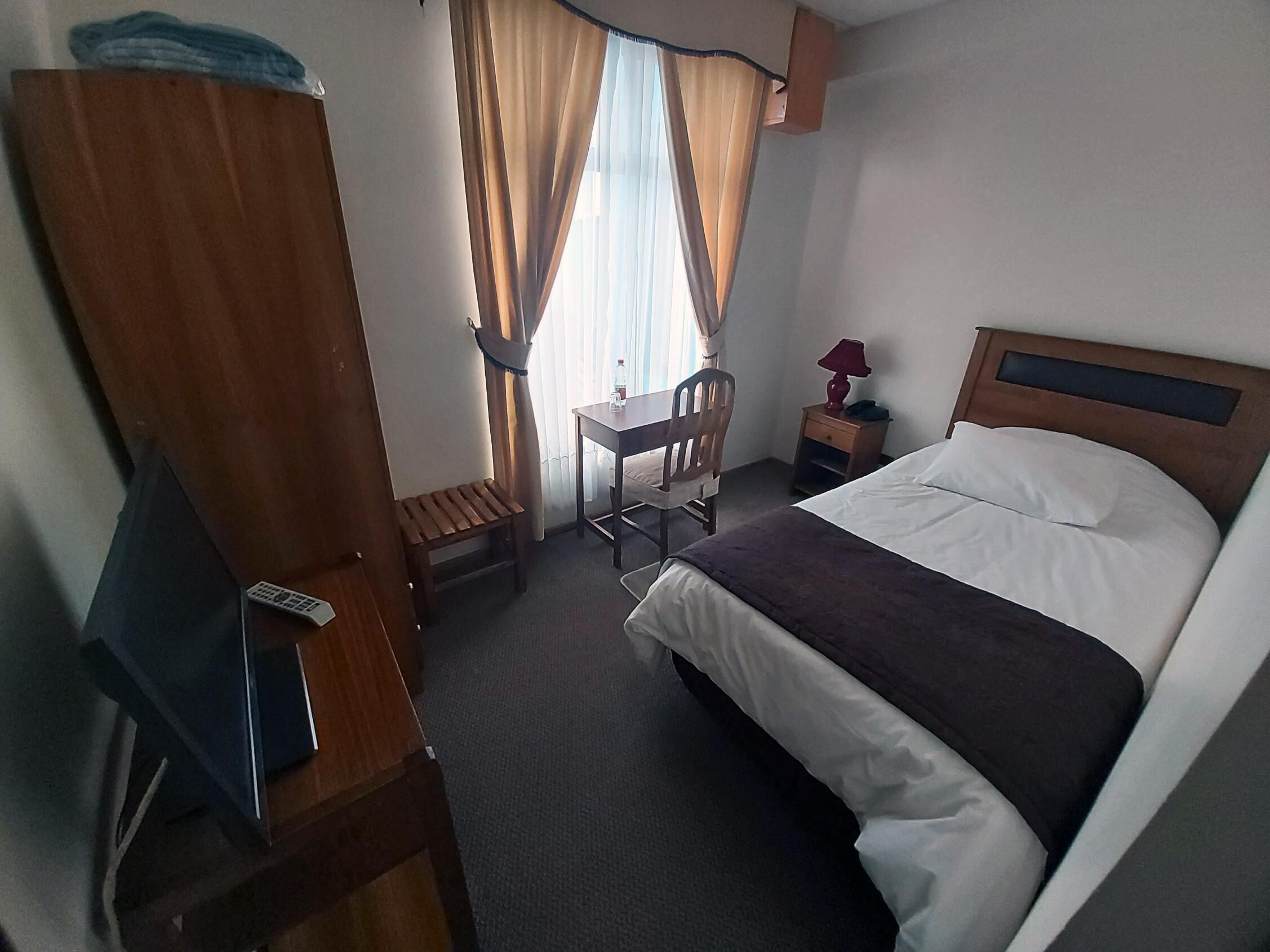 A hotel room with a bed, a desk, a chair, a nightstand, and a TV.