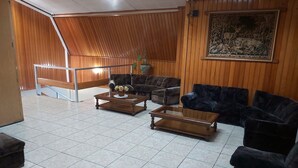 A spacious living area with a high ceiling, wooden paneling, and a large wall-mounted artwork. There are multiple seating options including sofas and armchairs, and a coffee table with a floral arrangement. - Hotel Esmeralda (Castro)
