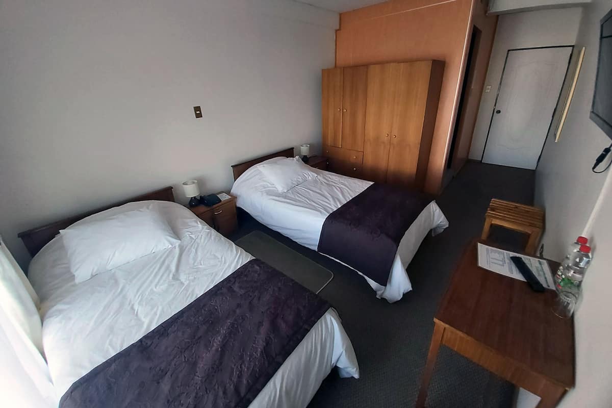 Habitación de hotel con dos camas, un armario de madera, un escritorio pequeño con una silla y una puerta.