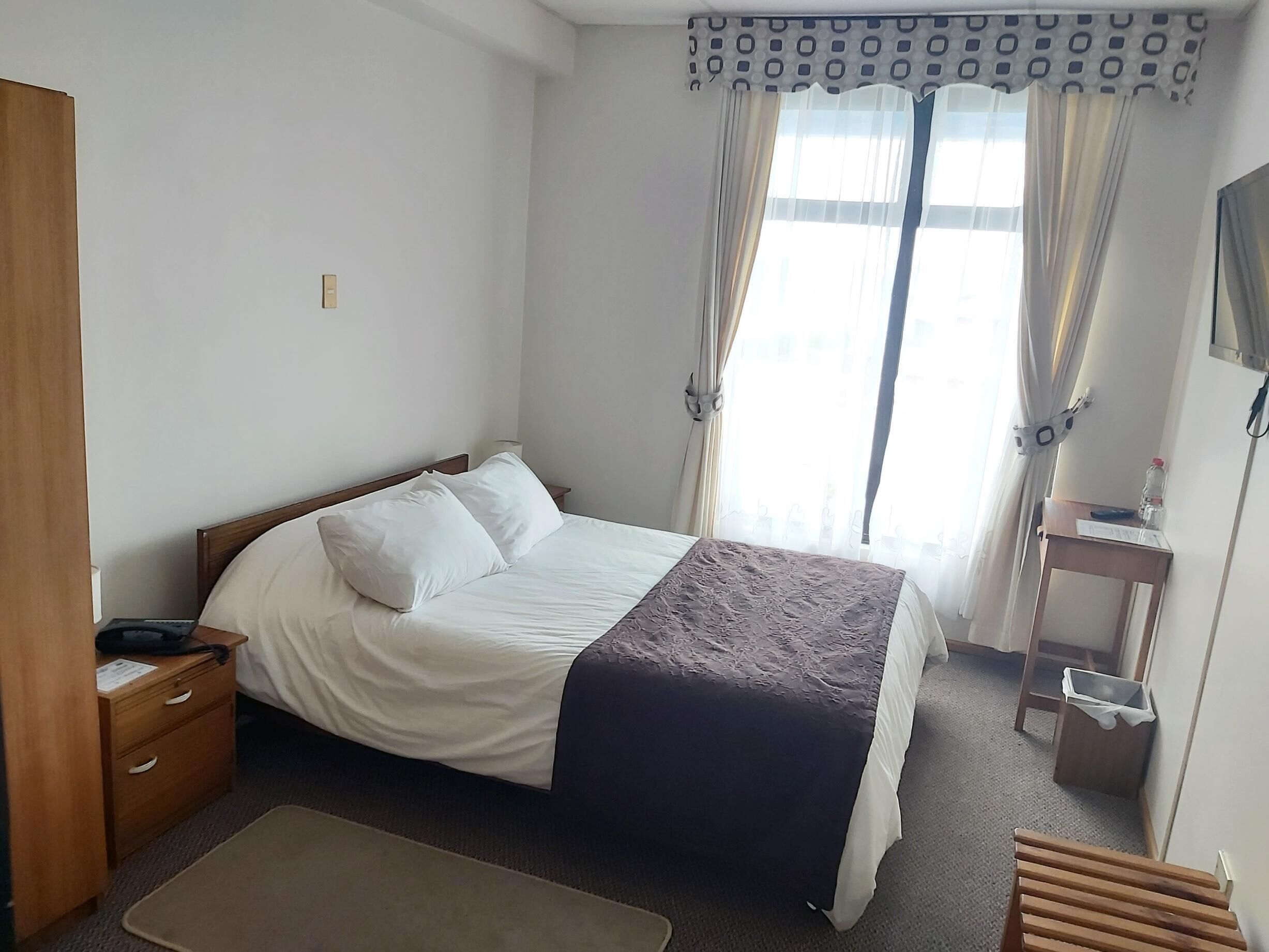 A neatly arranged hotel room with a bed, bedside table, and a small desk with a chair.