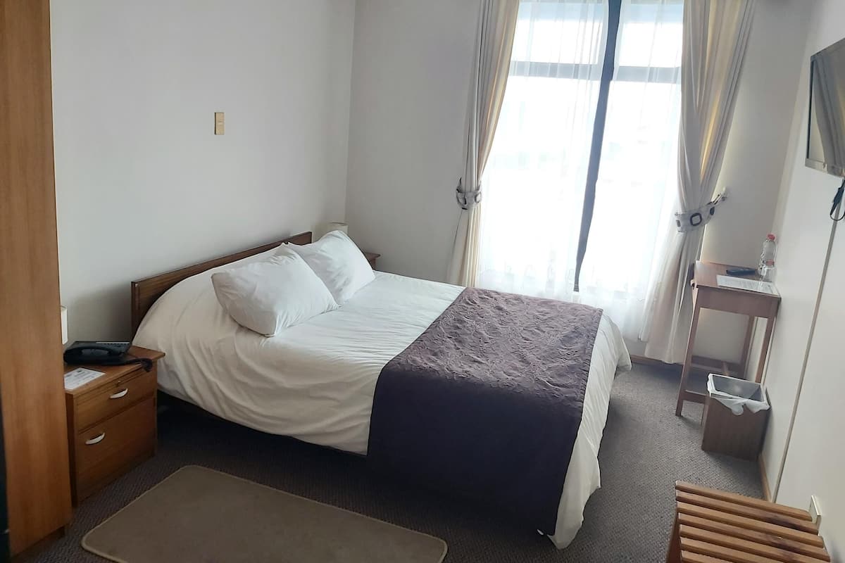 Una habitación de hotel ordenada con una cama, una mesita de noche y un pequeño escritorio con una silla.