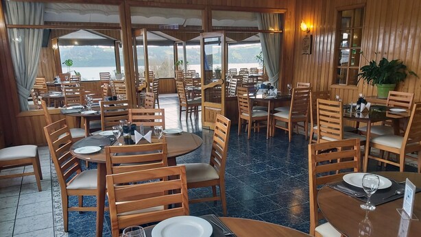 A restaurant with wooden furniture and a view of the sea. Tables are set with plates, glasses, and cutlery. - Hotel Esmeralda (Castro)