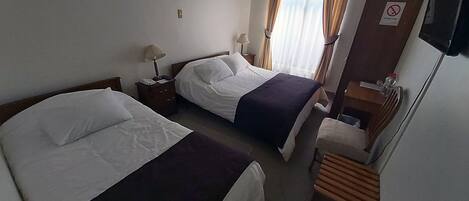 A hotel room with two beds, a desk, a chair, a TV, and a window with curtains.