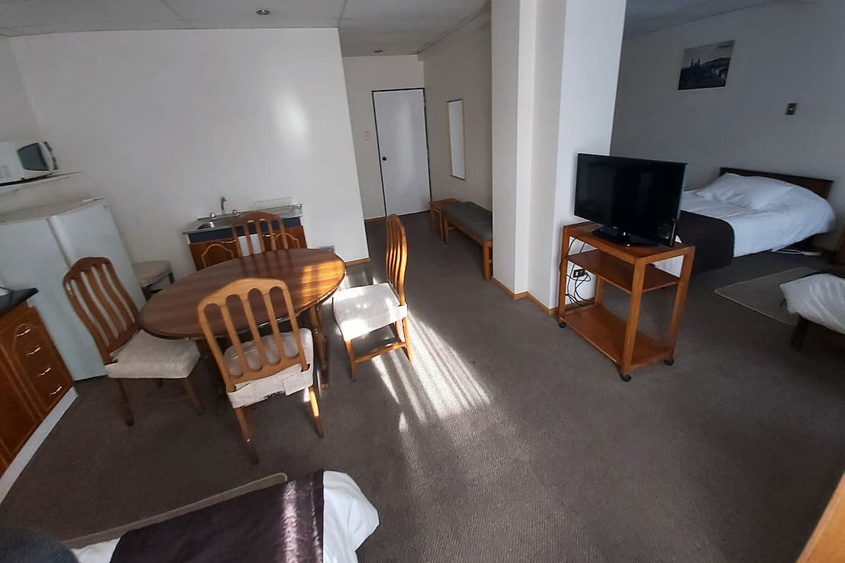 Habitación de hotel con una mesa de comedor, sillas, televisor sobre un mueble, cama y una pequeña kitchenette.