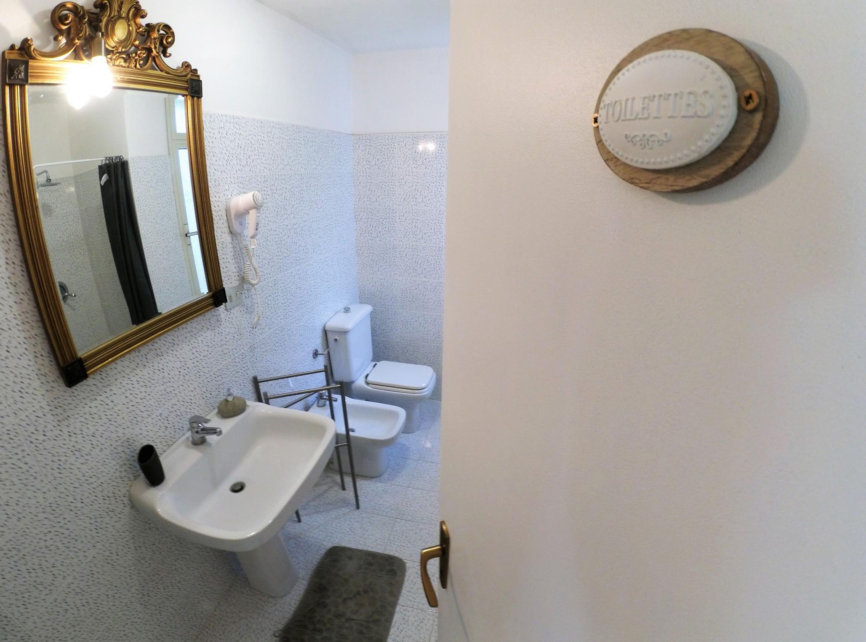 Une salle de bain avec un lavabo blanc, des toilettes et un miroir doté d’un cadre orné.