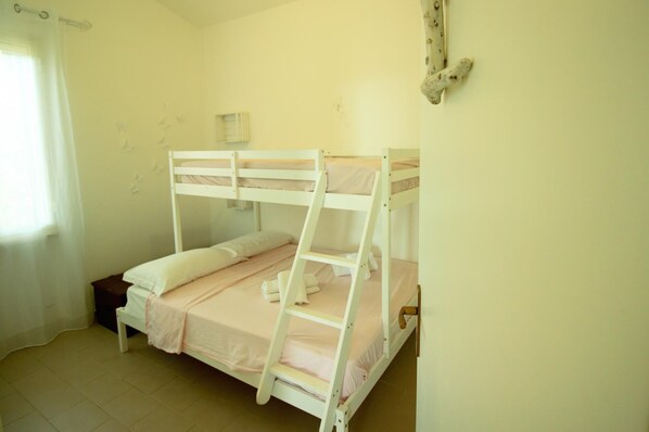 A bunk bed room with a window, a small bedside table, and a wall-mounted shelf.
